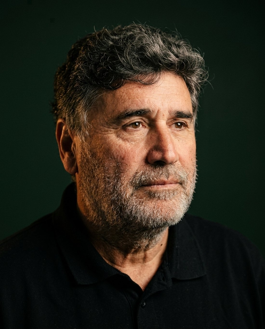 Retrato de Ronald Pool, hombre chileno de unos cincuenta y cinco años, pelo canoso y rizado y barba gris, con polera negra, girado levemente y con gesto sereno de quien escucha.